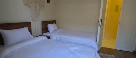 A room with two beds, wooden headboards, a macrame wall hanging, and an air conditioning unit.