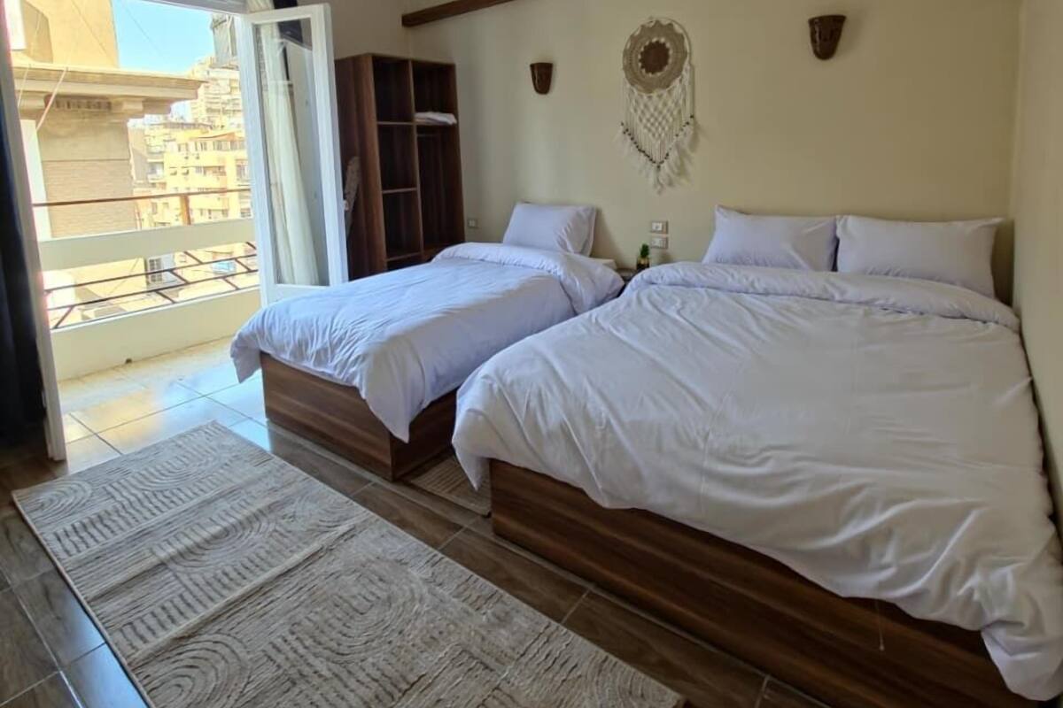 A hotel room with two beds, a large window, a wardrobe, and a decorative wall hanging.