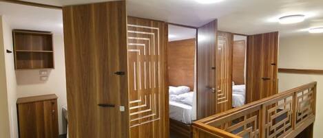 A hotel room with a wooden wardrobe, a bed, a small cabinet, and a staircase with a wooden railing.