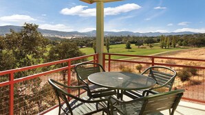 Varanda com mesa e cadeiras, vista para um campo de golfe e montanhas ao longe.