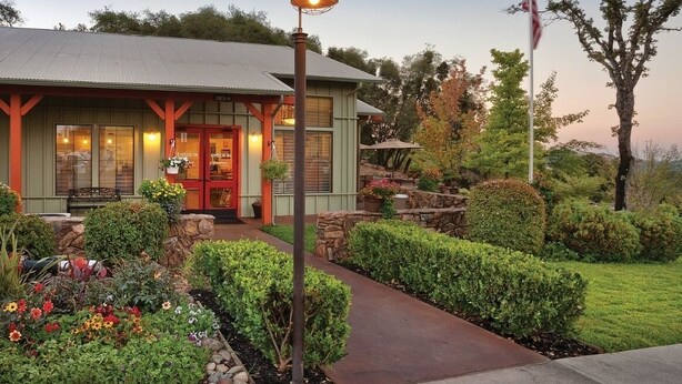 Um edifício com fachada verde, porta vermelha e um jardim bem cuidado com diversas plantas e flores.