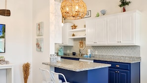A kitchen with white cabinets, a blue island, and a hanging light fixture. - 40th Street Cottage (Port St. Joe)
