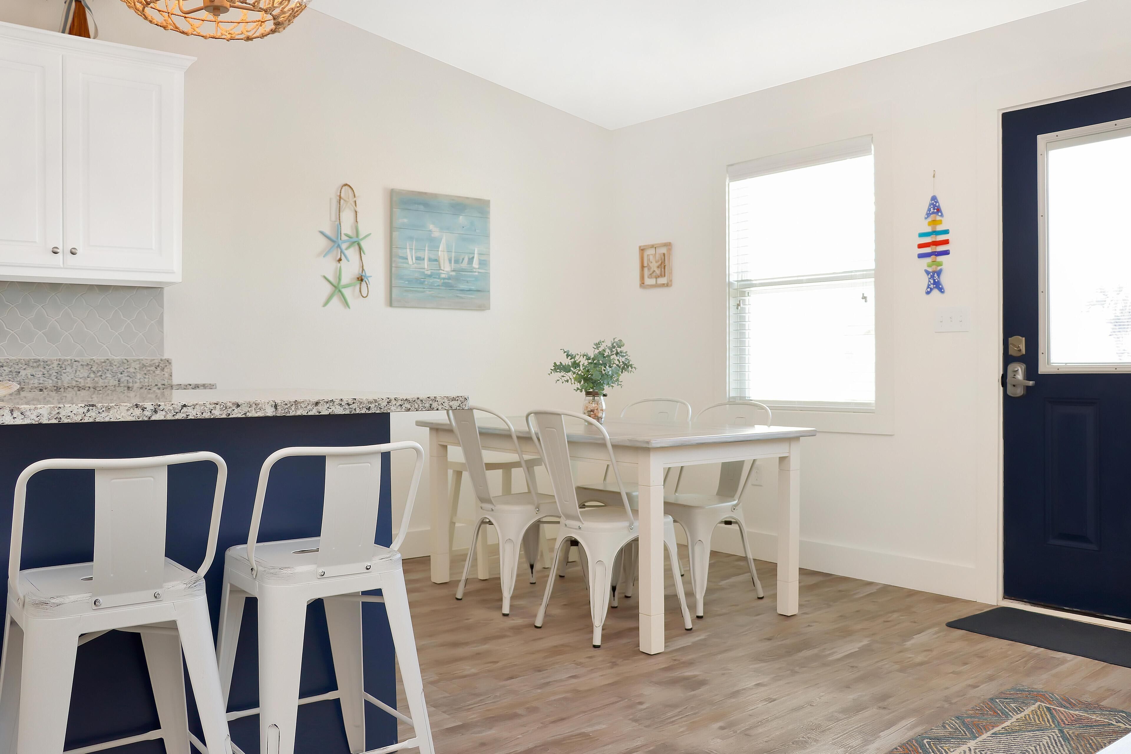 A kitchen with white cabinets, a granite countertop, a dining table with white chairs, and a dark blue door.
