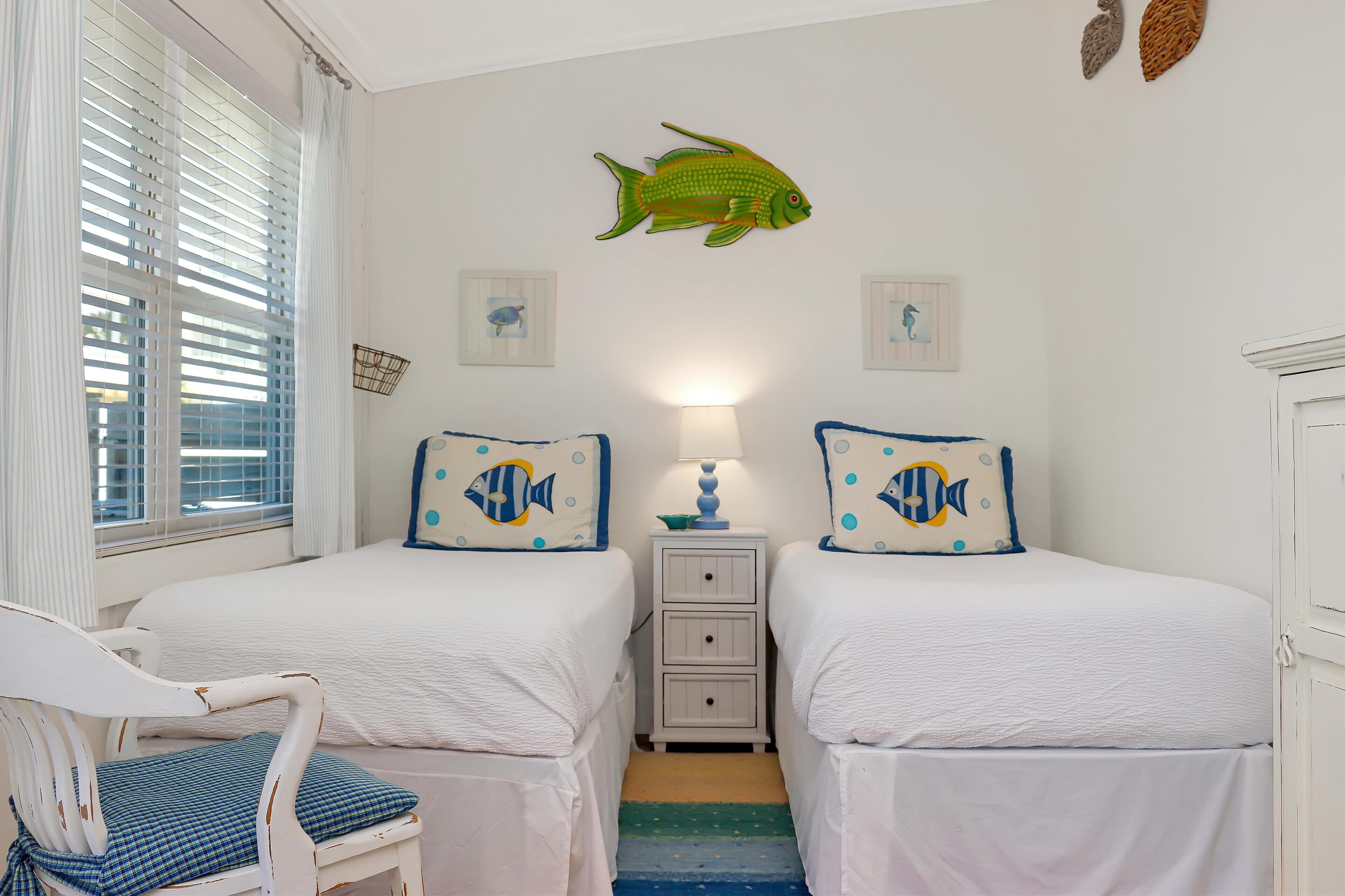 Ein Schlafzimmer mit zwei Betten, einem Nachttisch, einem Sessel und einer Fisch-Wanddekoration.