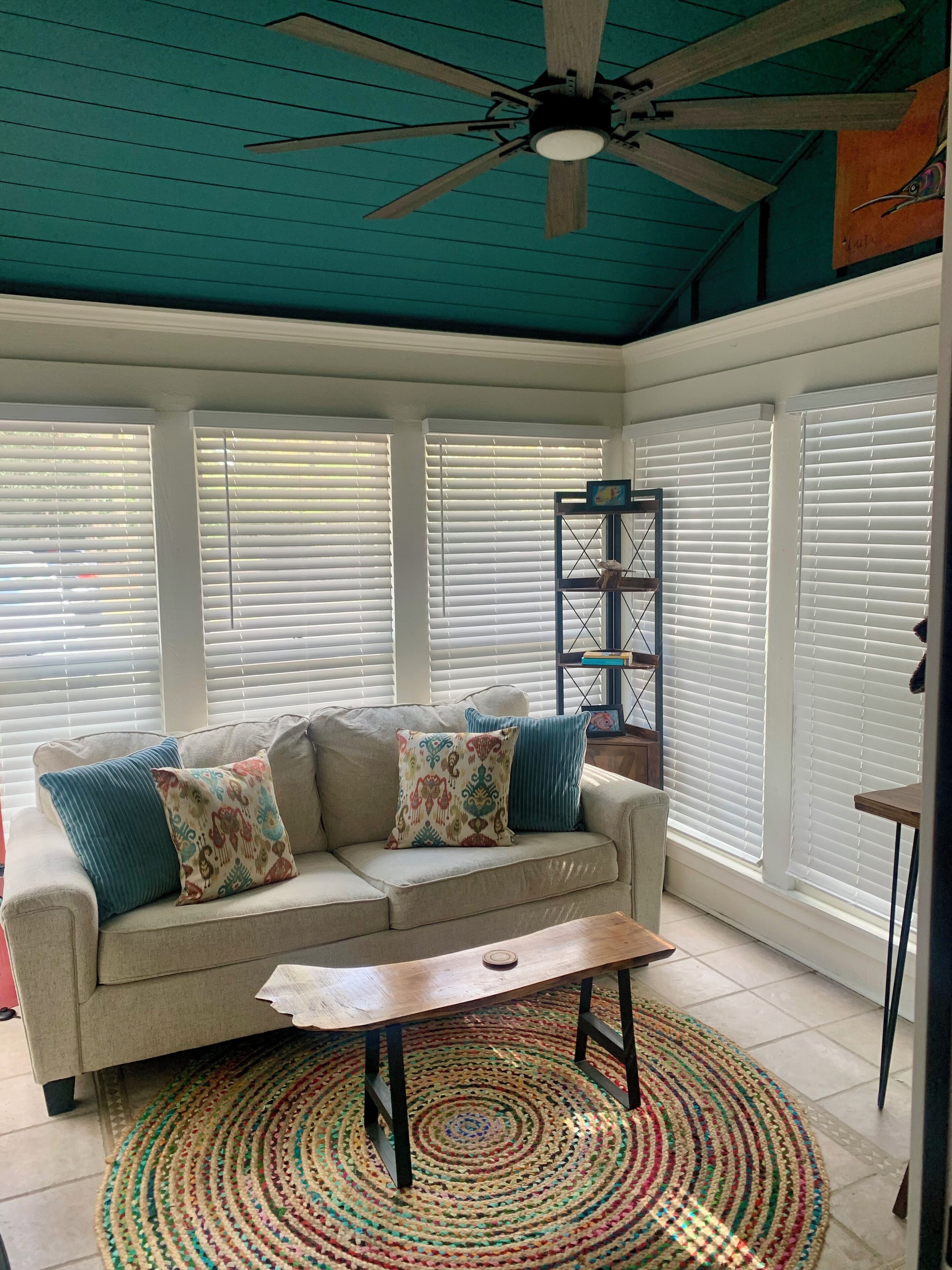 Une pièce avec un canapé beige, des coussins colorés, une table basse en bois, un tapis à motifs et un ventilateur de plafond.