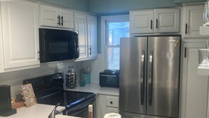 A modern kitchen with white cabinets, a stainless steel refrigerator, a microwave, and a stove. - The Hil & Dale: Wayside Forest UNIT 12. Entire Townhouse. Pets welcomed! (Murrells Inlet)