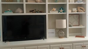 A white entertainment center with a flat-screen TV, decorative items, and a lamp. - The Hil & Dale: Wayside Forest UNIT 12. Entire Townhouse. Pets welcomed! (Murrells Inlet)