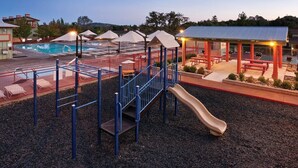 Ein Spielplatz mit Rutsche und Klettergerüsten, einem Pool und einem überdachten Pavillon mit Bänken.