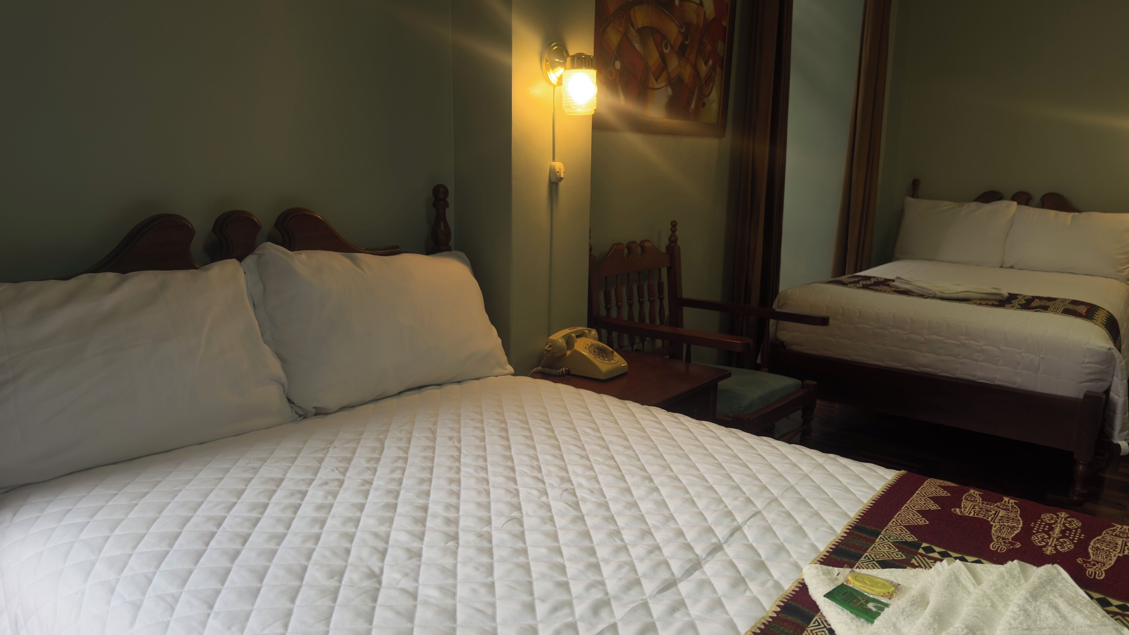 A hotel room with a large bed, a bedside table with a telephone, and a wall-mounted light fixture.