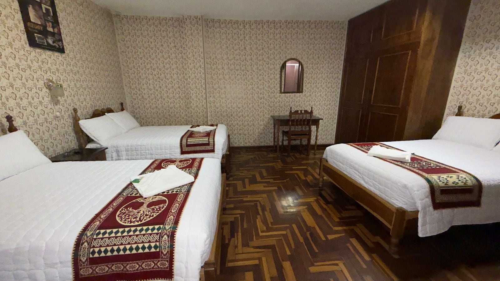 Habitació d'hotel amb dos llits, un sòl de fusta i una taula petita.