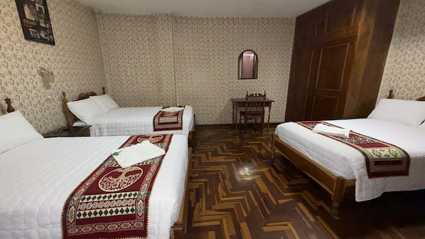A hotel room with two beds, a wooden floor, and a small table.