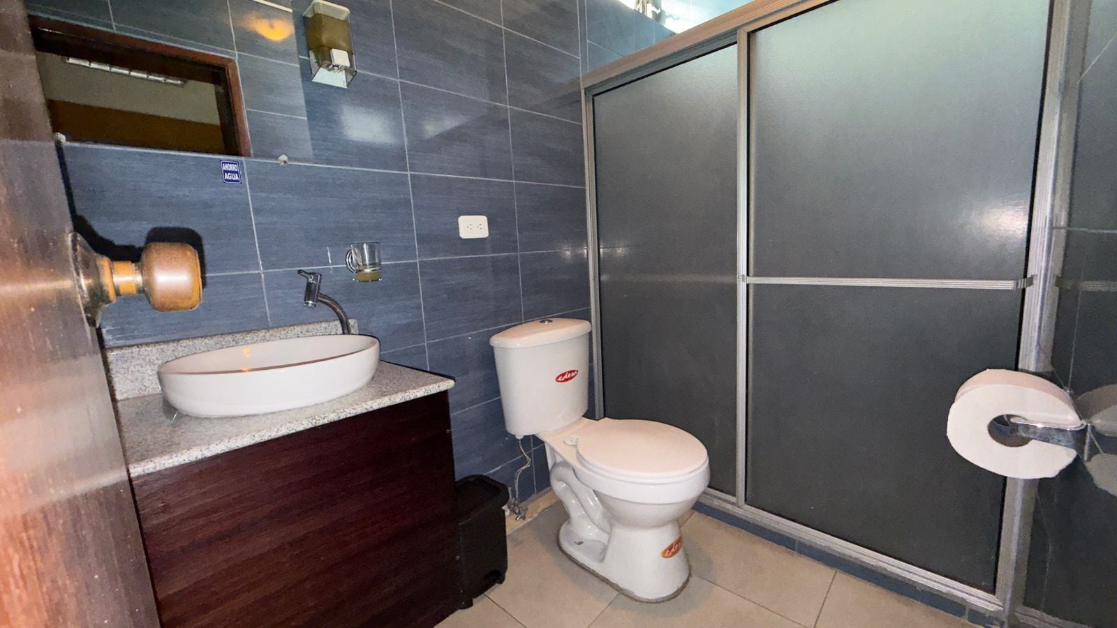 A bathroom with a white sink, dark wooden vanity, a white toilet, and a glass shower enclosure.