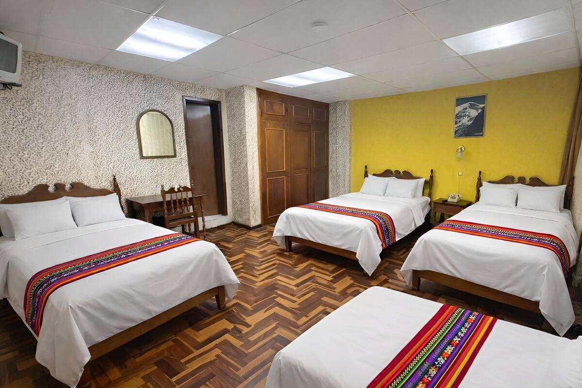 A hotel room with two beds, a wooden floor, a mirror, a door, and a yellow wall.