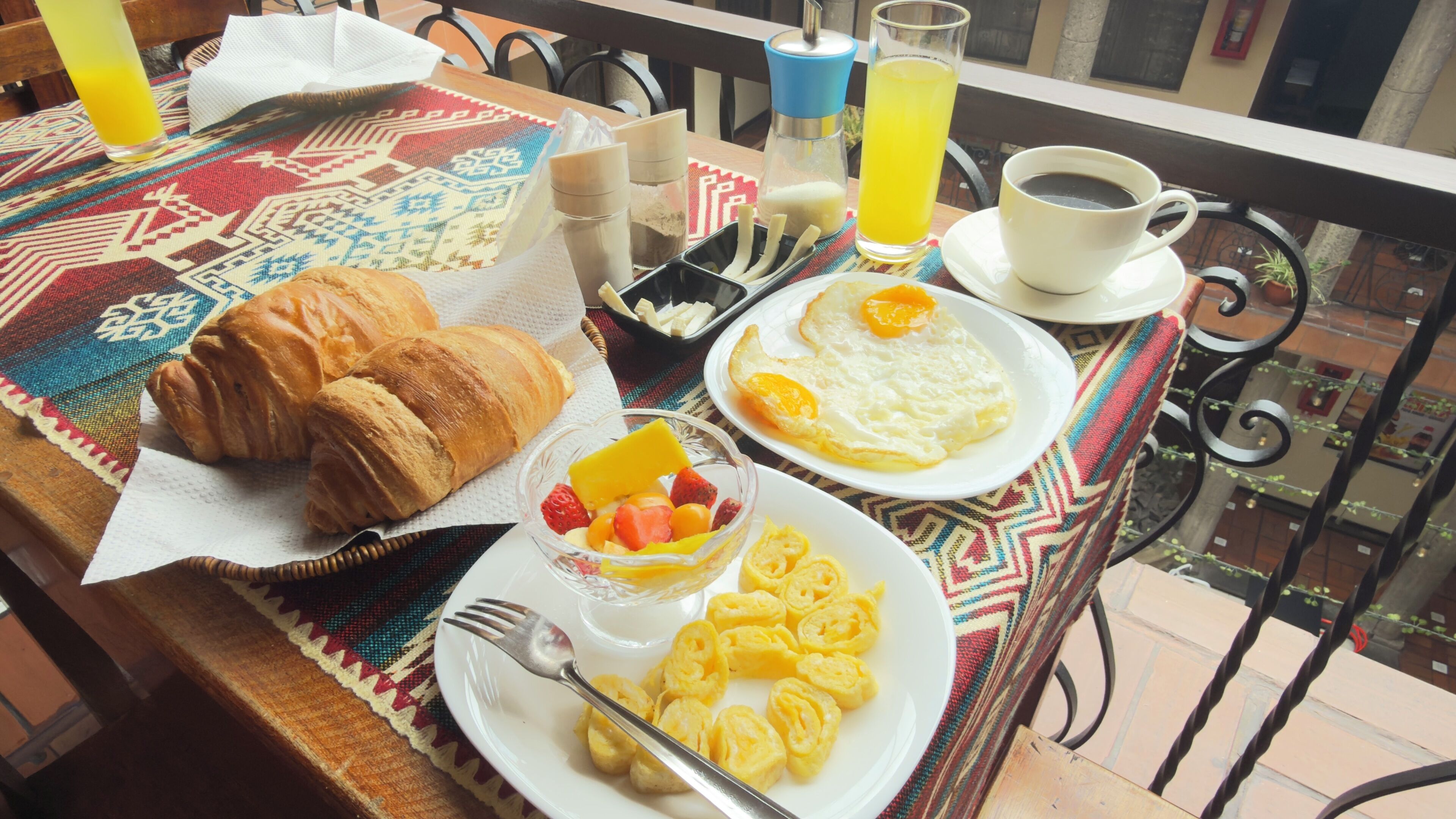 Une table de petit-déjeuner avec des croissants, des fruits, des œufs brouillés, du café et du jus de fruits.