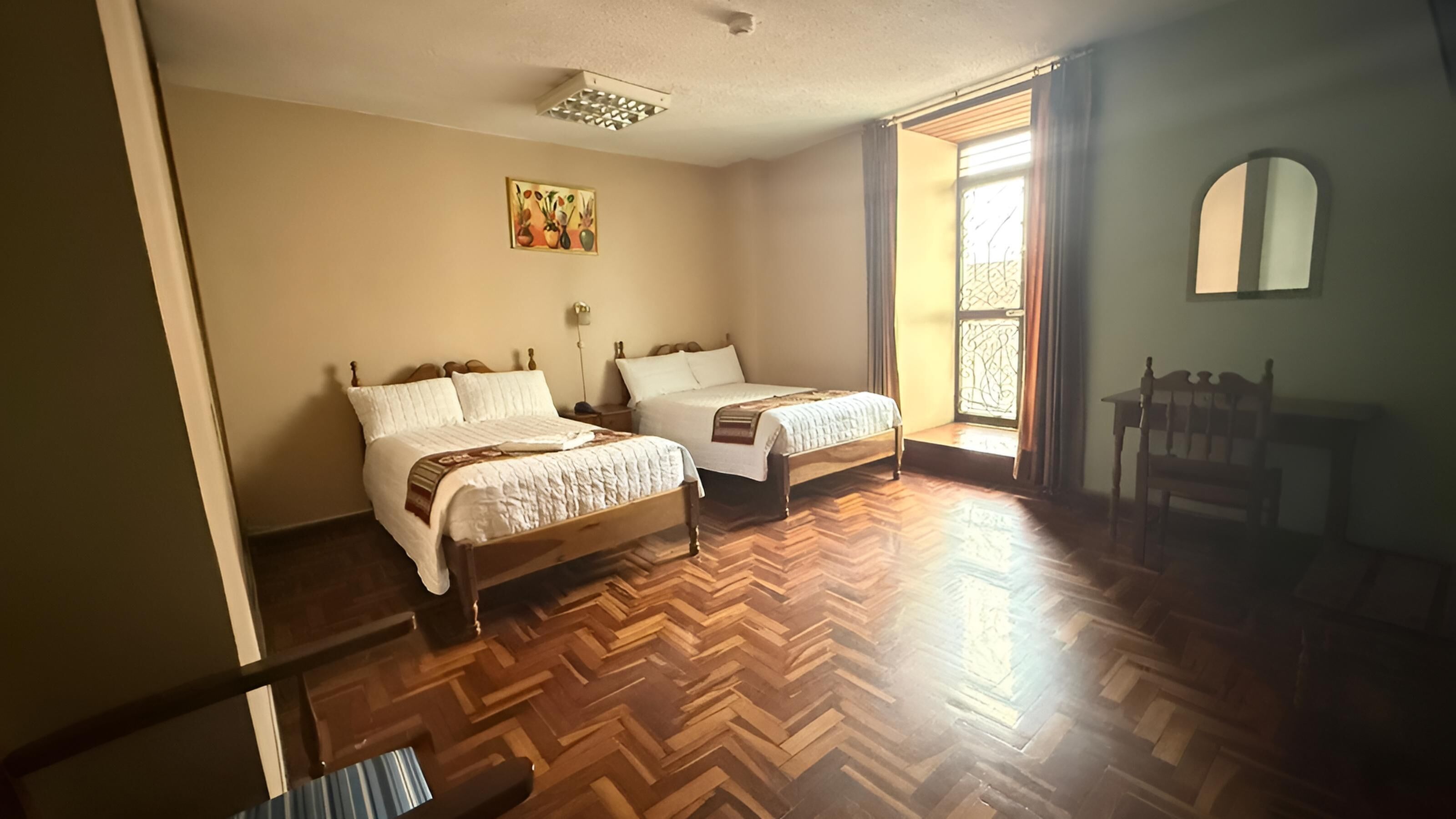 Une chambre avec deux lits, un plancher en bois, une fenêtre avec des rideaux, une chaise et un tableau au mur.