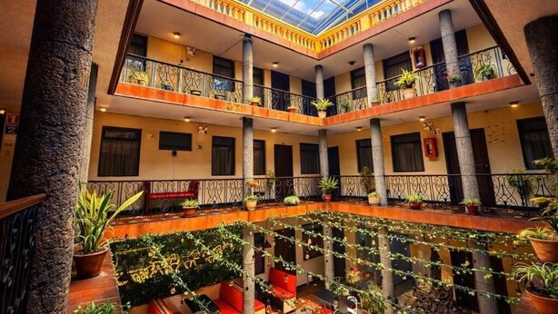 A multi-level atrium with a glass ceiling, columns, and potted plants. - Hostal Viena Internacional (Quito)
