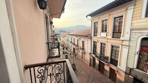 A balcony with a wrought iron railing overlooking a street lined with colorful buildings. - Hostal Viena Internacional (Quito)