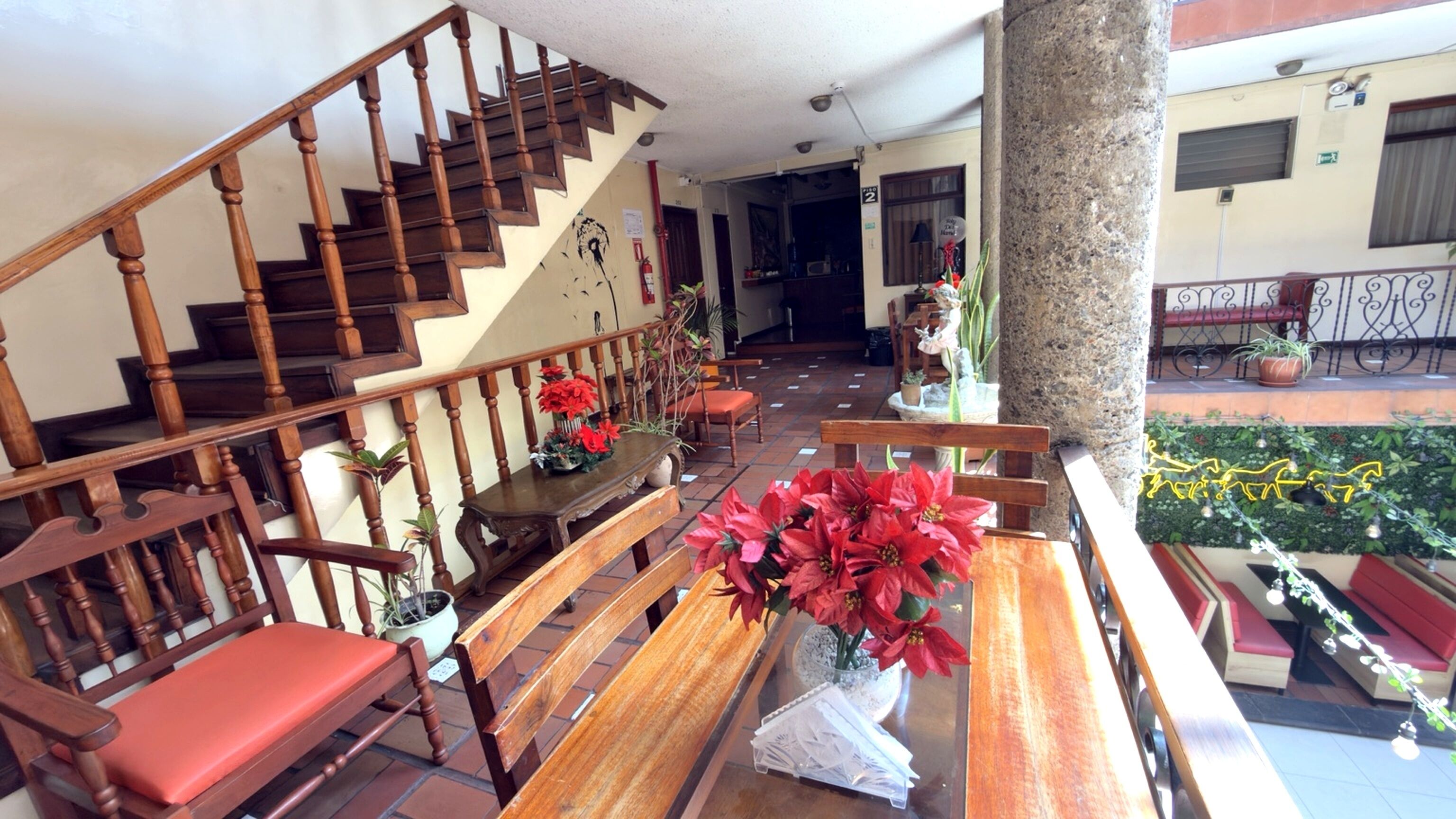 A hotel lobby with wooden benches, a staircase, and a large tree.