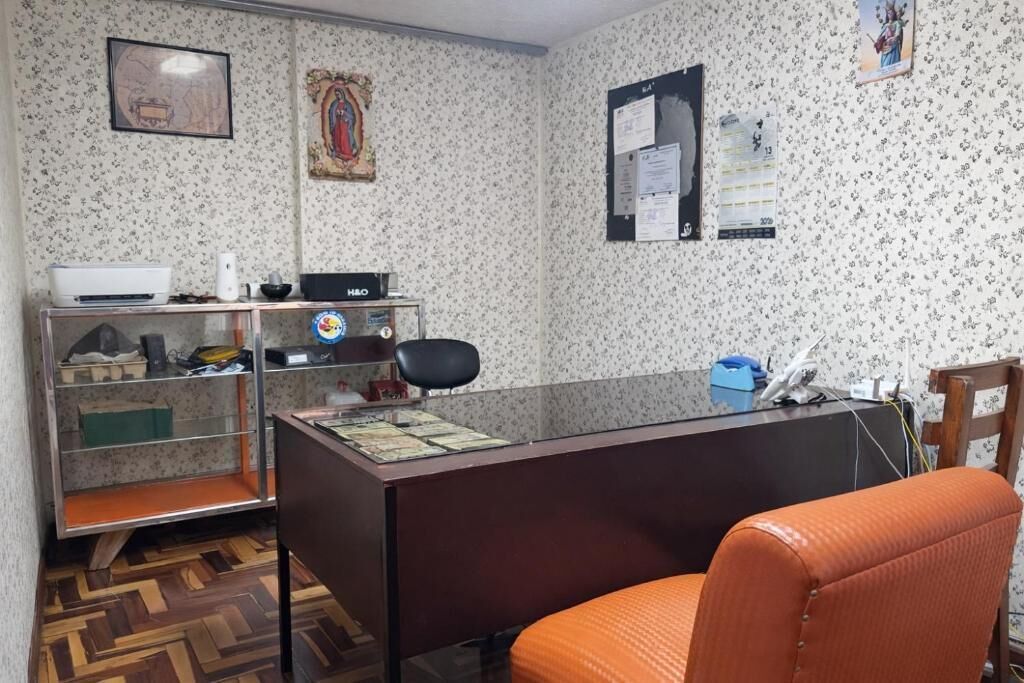 A room with a wooden herringbone floor, a desk with a computer, a chair, and a shelf with various items.