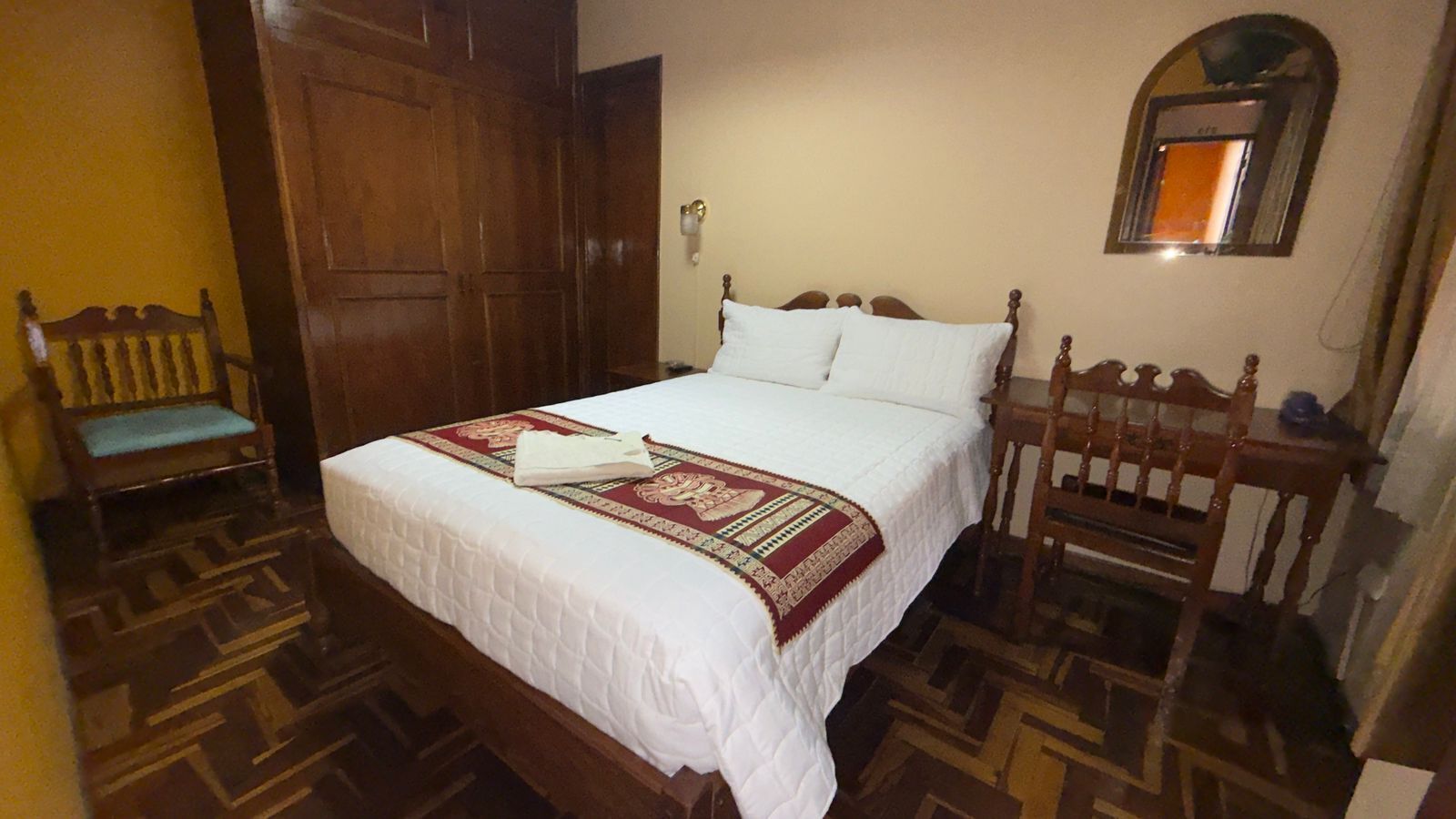Un dormitorio con una cama de madera, un banco y un espejo en la pared.