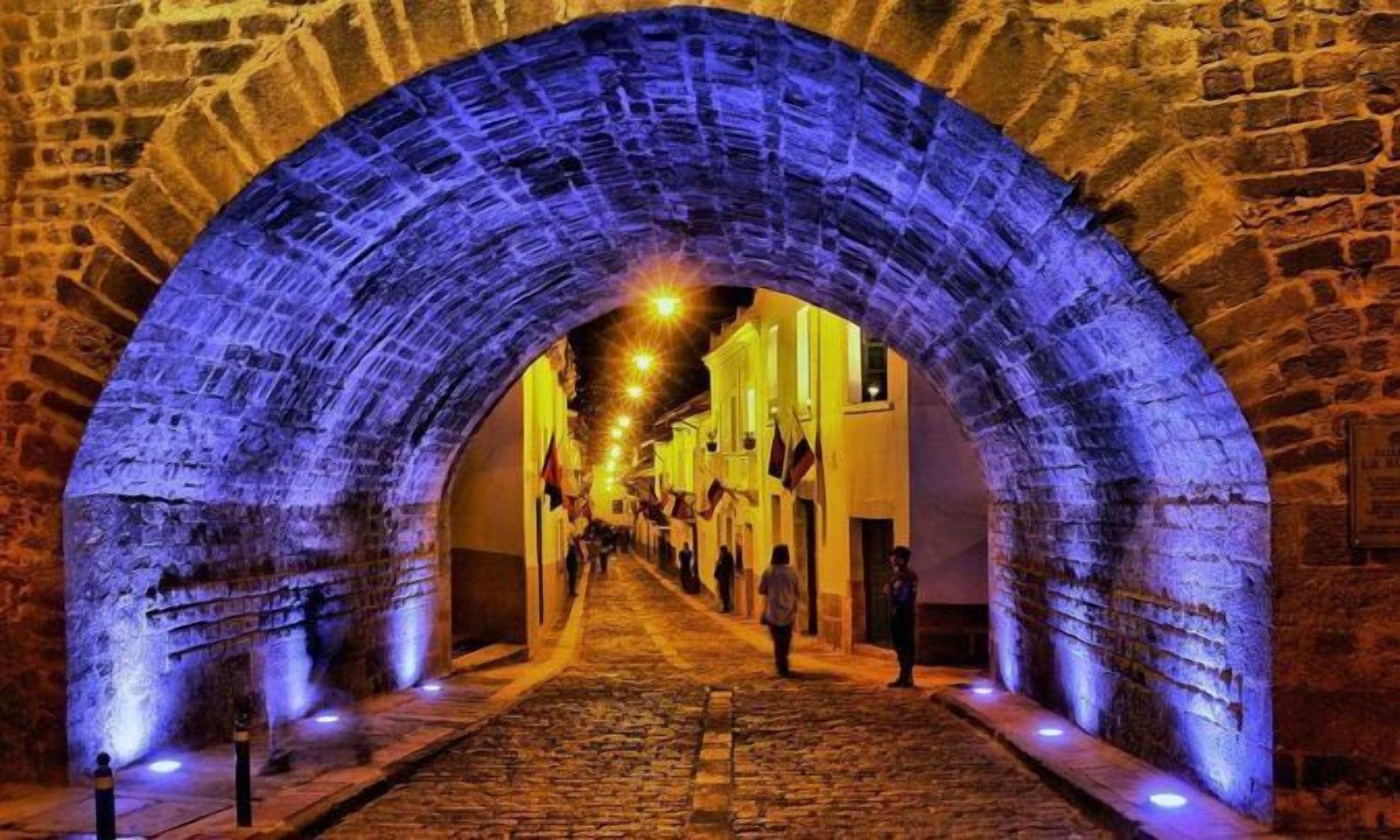 A stone archway leading into a cobblestone street with people walking.