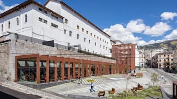 A modern building with a white facade, large windows, and a courtyard with benches and greenery.