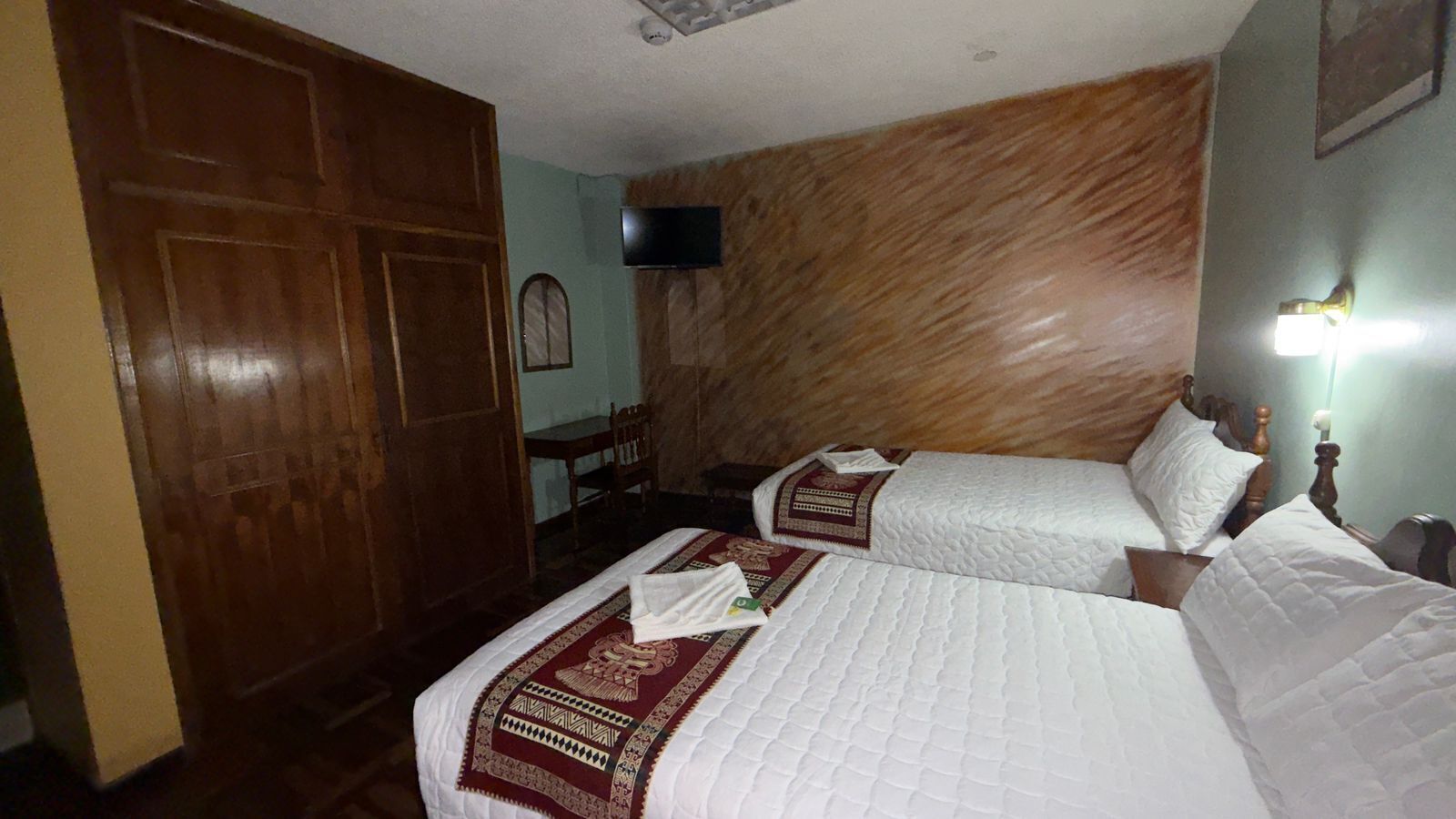 Ett hotellrum med två sängar, en garderob i trä, en tv och ett skrivbord med en stol.
