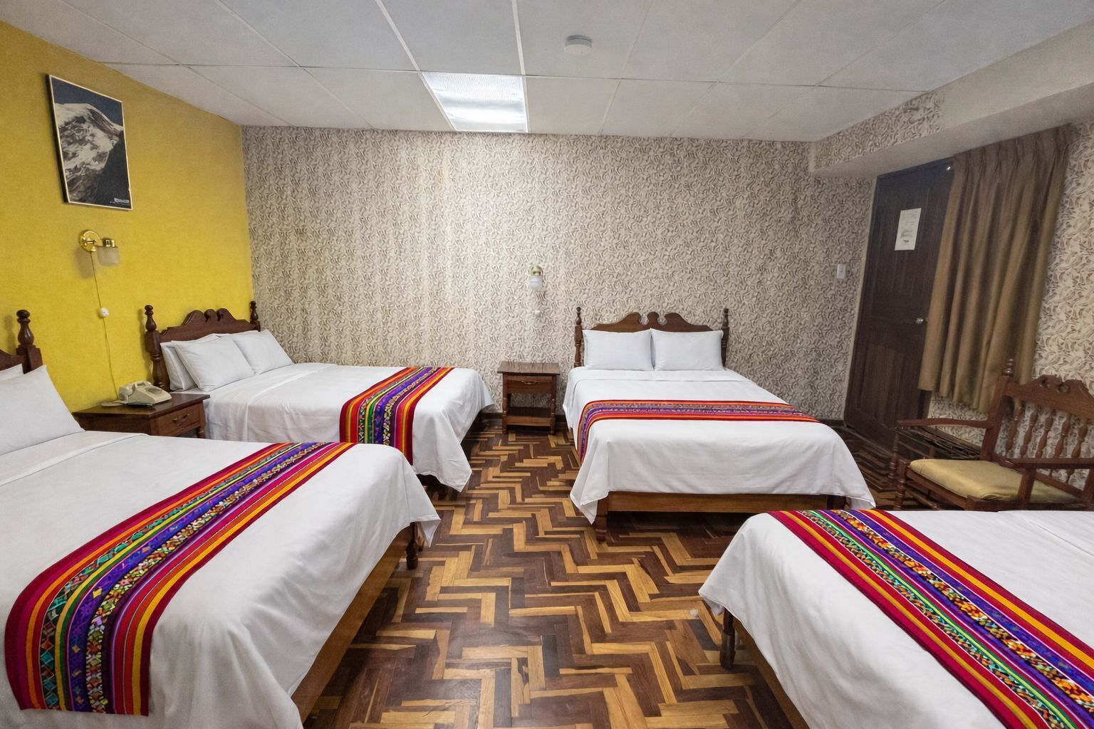 Une chambre d’hôtel avec trois lits, un plancher en bois, un mur à motifs et un mur d’accent jaune.