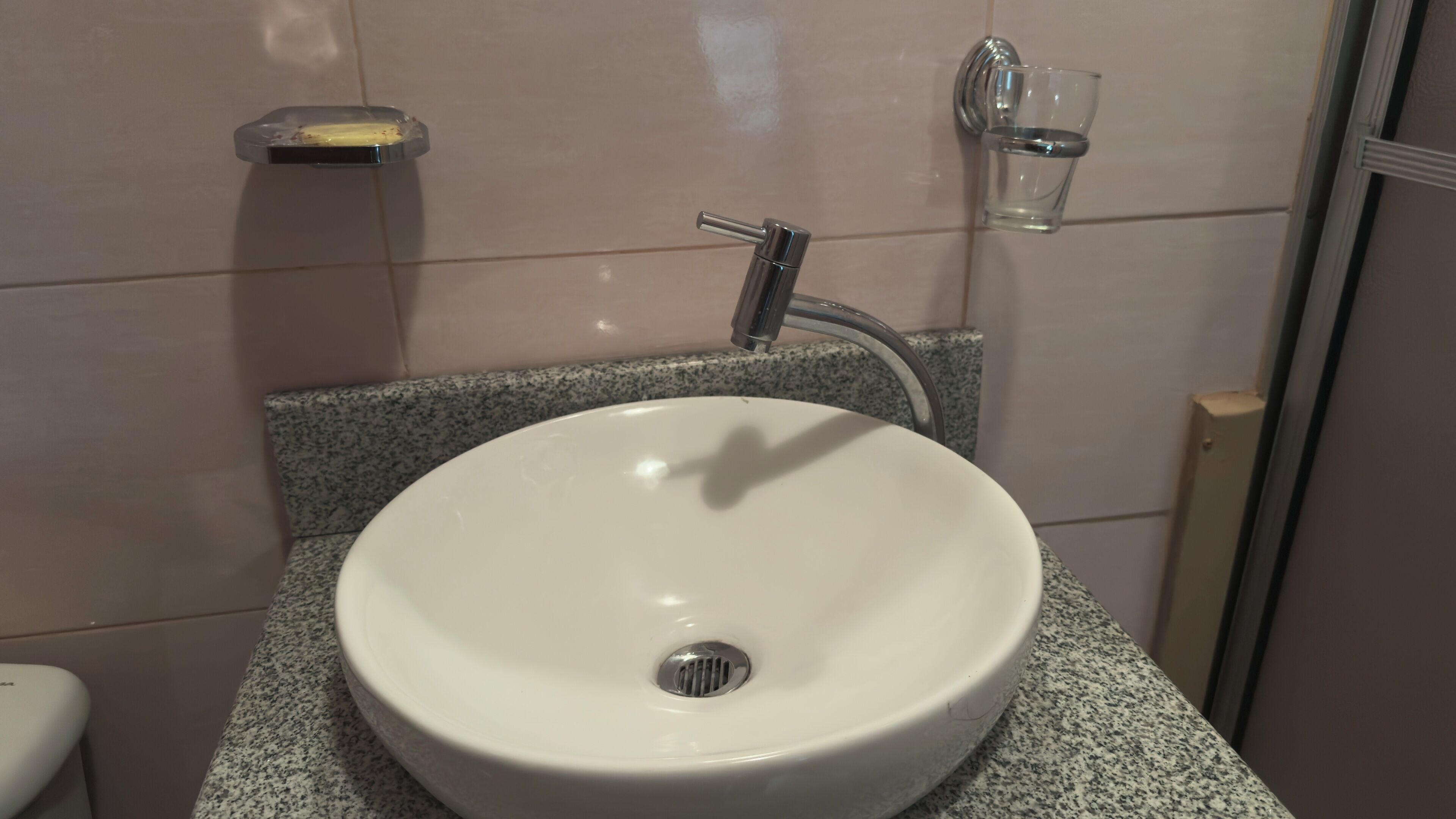 Ein Badezimmer mit einem weißen Waschbecken, einem Wasserhahn, einer Seifenschale und einem Glas Wasser.