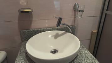 Ein Badezimmer mit einem weißen Waschbecken, einem Wasserhahn, einer Seifenschale und einem Glas Wasser.