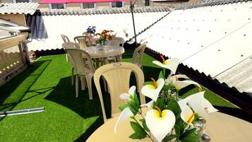 An outdoor patio with a round table, chairs, a small garden area with artificial grass, and a large umbrella providing shade.