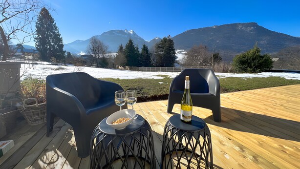Eine Terrasse mit zwei Stühlen, einem Tisch, einer Weinflasche und zwei Gläsern.