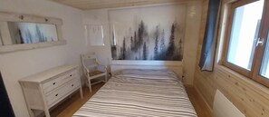A bedroom with a bed, a dresser, a chair, a painting of trees, and a window. - Gite Cairn, ground floor chalet near Lake Annecy and ski resorts (Faverges)