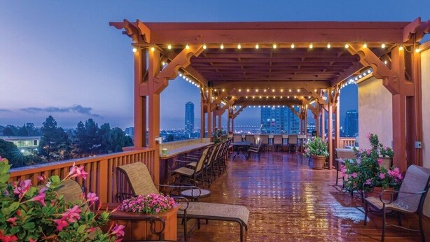 A covered outdoor seating area with chairs and tables, string lights, and potted plants.