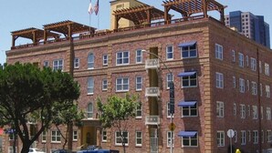 A multi-story brick building with a balcony on the second floor, a flag, and a fire hydrant in front.