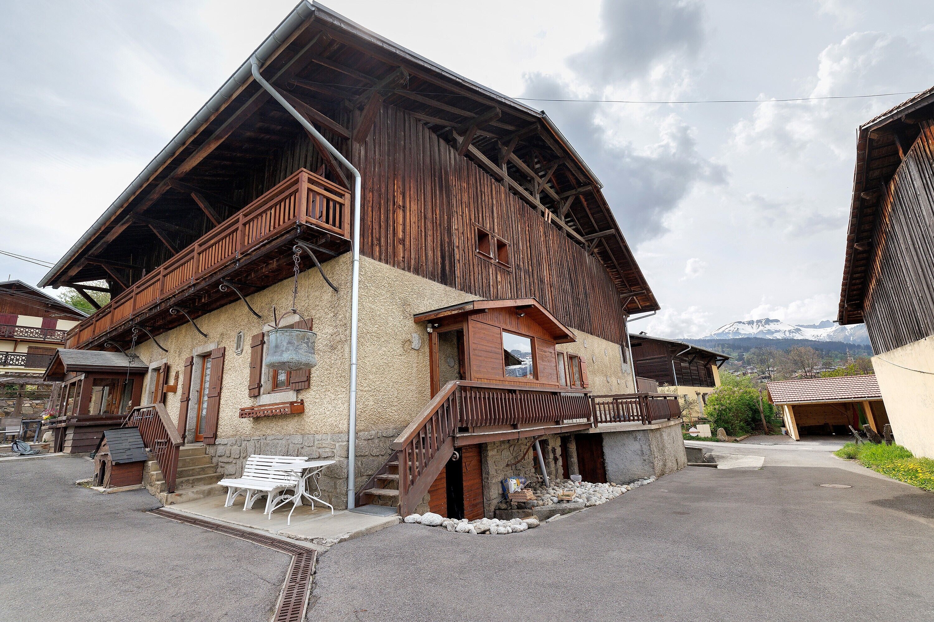Un bâtiment traditionnel en bois, doté d’un balcon, d’un escalier et offrant une vue sur les montagnes en arrière-plan.