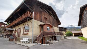 Un bâtiment traditionnel en bois, doté d’un balcon, d’un escalier et offrant une vue sur les montagnes en arrière-plan.