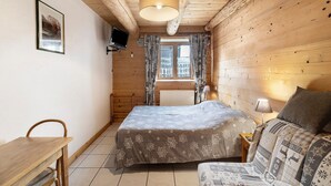 A wooden cabin bedroom with a bed, a sofa, a TV, and a window with curtains. - Bed and Breakfast 'La Ferme Du Mont Blanc - Vallot' with Mountain View (Combloux)