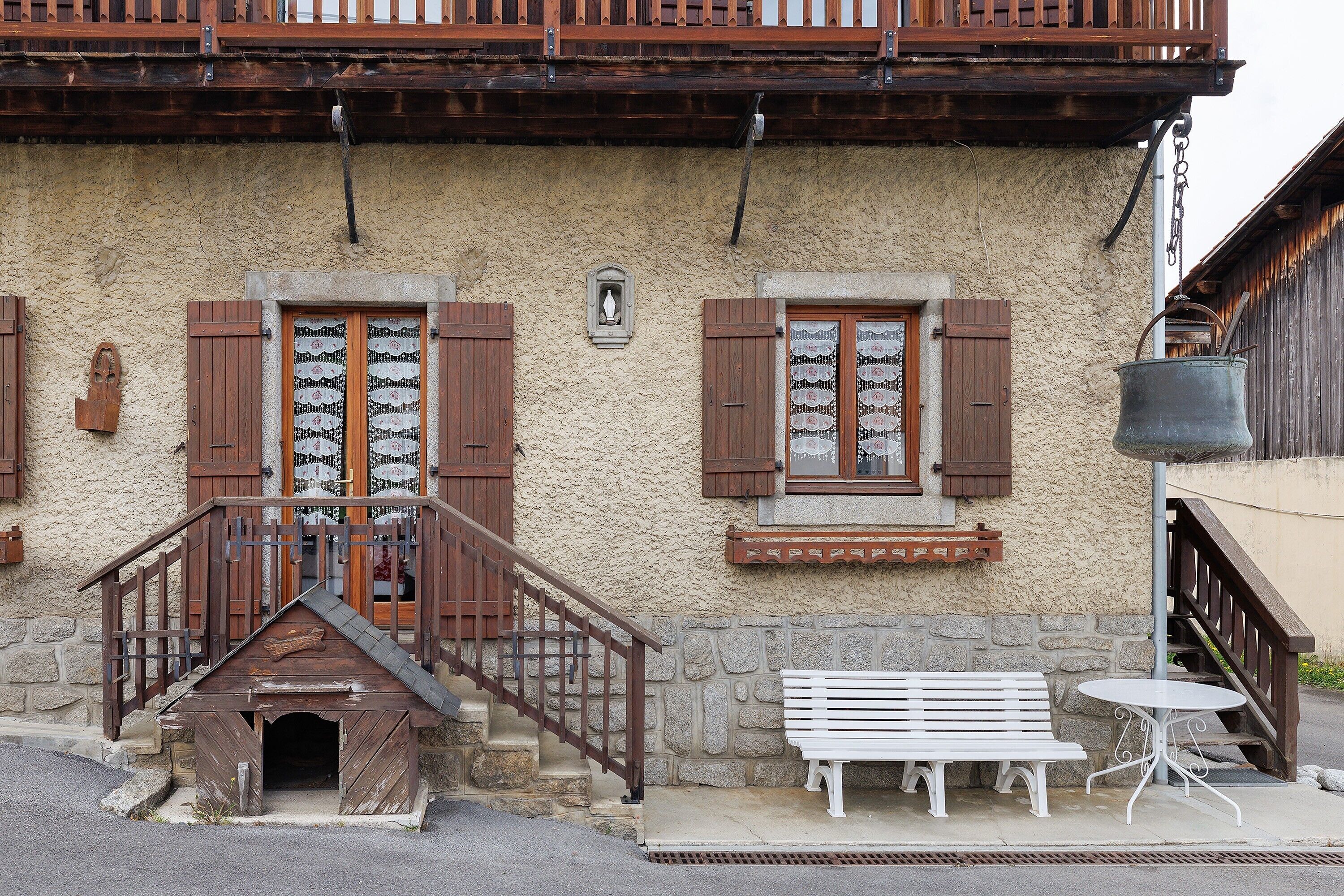 Un edificio rustico con persiane in legno, una cuccia per cani, una panchina e un tavolo.