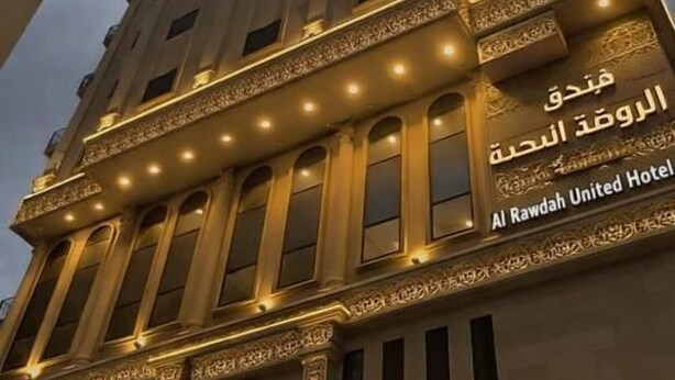 Un edificio alto con letreros iluminados que indican Al Rawdah United Hotel.