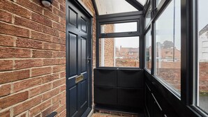 A narrow corridor with a black door and a window leading to a brick exterior. - Host & Stay | Bridge Court (Yarm)