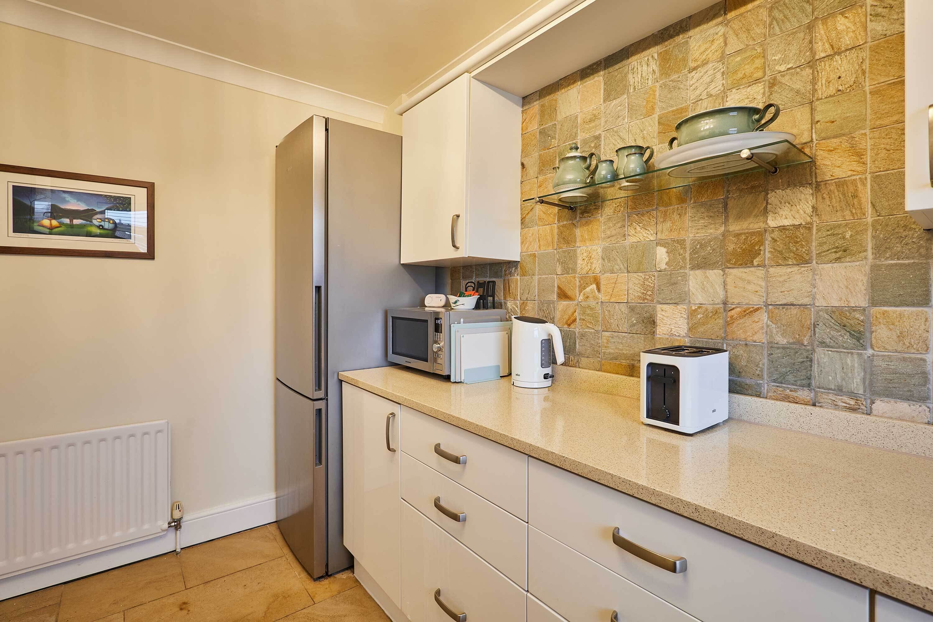 A kitchen with white cabinets, a microwave, a toaster, and a glass shelf with kitchenware.