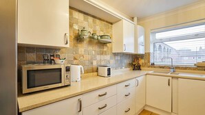 A modern kitchen with white cabinets, a granite countertop, a microwave, a toaster, and a window with blinds. - Host & Stay | Bridge Court (Yarm)