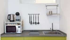 Une cuisine compacte équipée d’un micro-ondes, d’une bouilloire et d’une machine à café sur le plan de travail, d’un porte-ustensiles suspendu, d’une petite étagère avec une râpe et d’un évier avec un robinet.