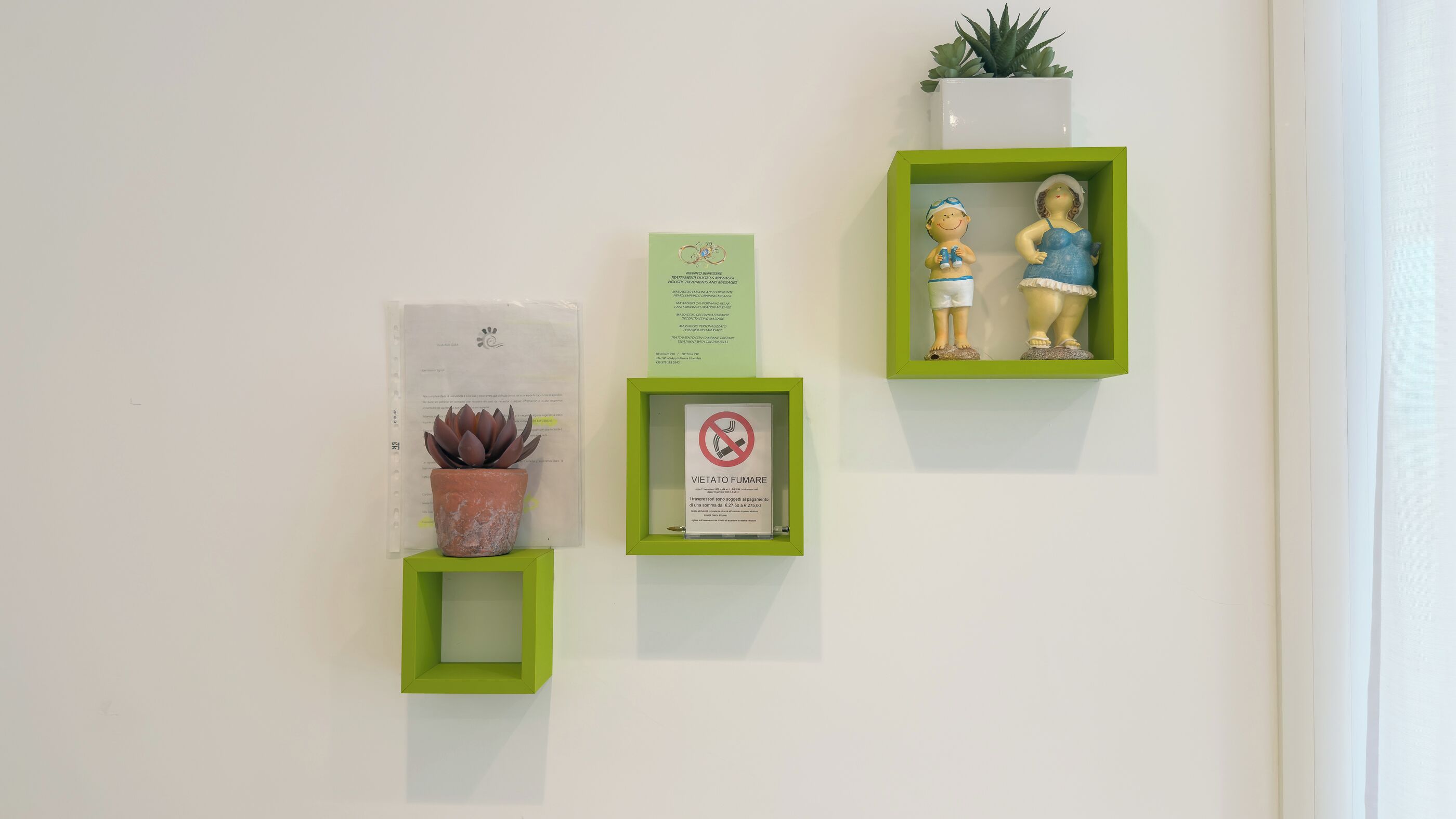 Uma parede com três elementos emoldurados em verde: uma suculenta em vaso, uma placa emoldurada e uma miniatura emoldurada de duas crianças.