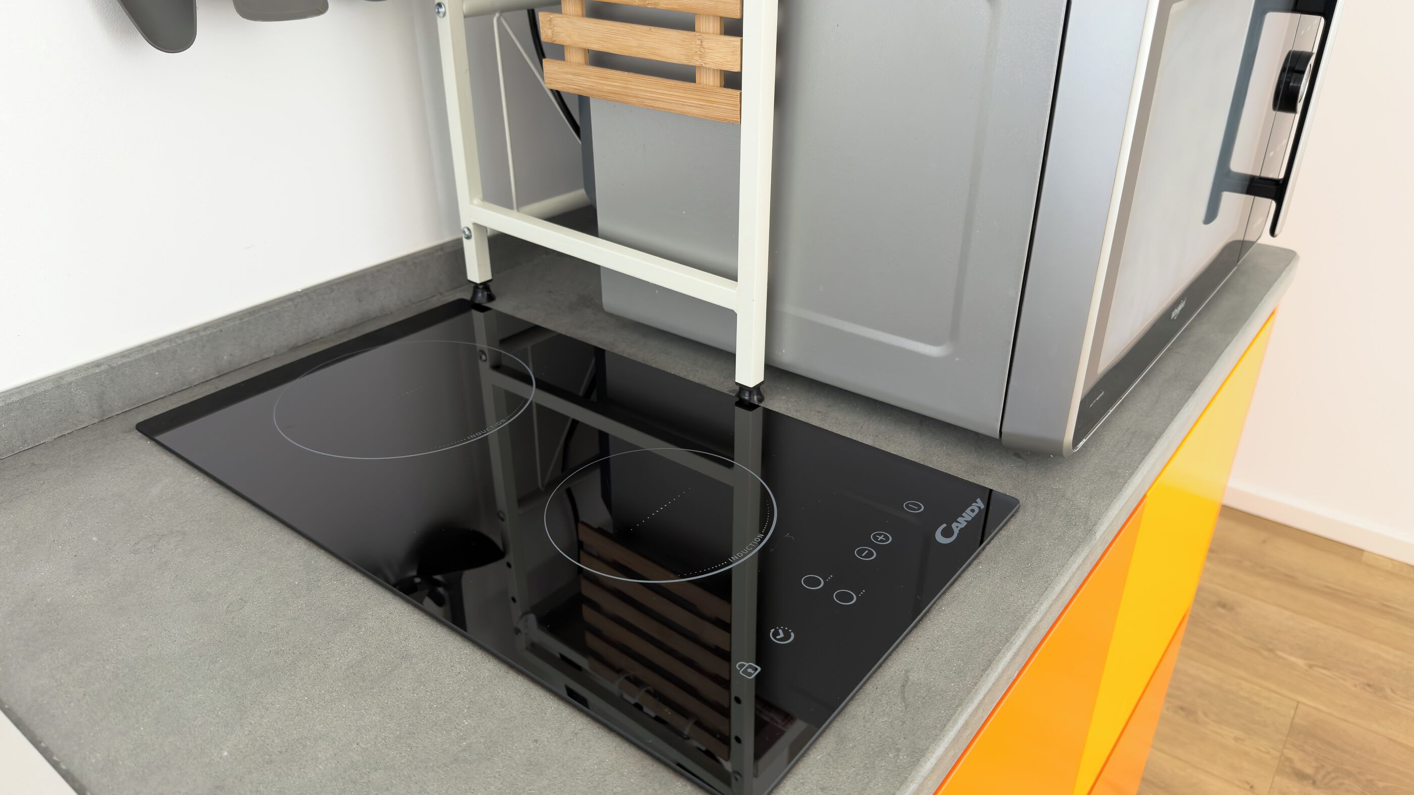 Una cocina con placa de inducción integrada, un estante de madera y electrodomésticos modernos.