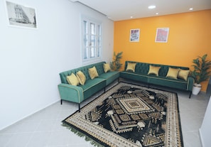 A living room with a green sectional sofa, a patterned rug, and two potted plants. - Hotel Karim Tunis (Tunis)