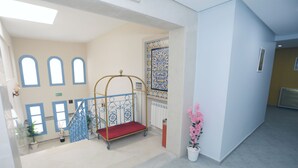 Un atrio di hotel con una scala, un carrello metallico, piante in vaso e un muro decorativo.