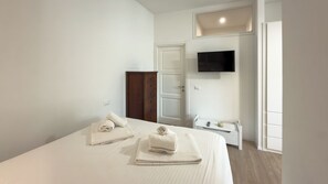 Une chambre à coucher comprenant un lit, deux oreillers, une armoire en bois, un téléviseur et une table de chevet avec une télécommande.
