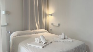 A hotel room with two beds, white linens, a wall-mounted light, and a power outlet. - Villa Ada-Orazio - One Bedroom Apartment, Sleeps 2 (Olbia)